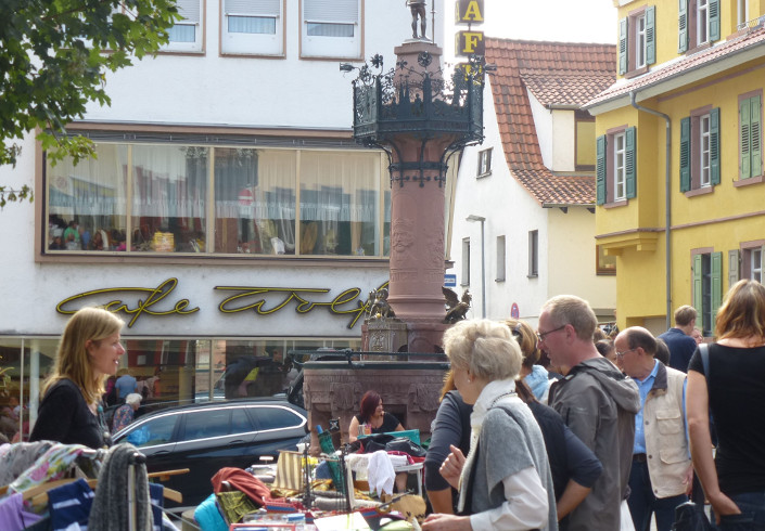 Flohmarkt in Weinheim, Flohmarktstand mit Menschen, die Gebrauchtes suchen und einer Frau, die Flohmarktstand betreibt